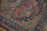 Meshed rug corner showing navy border, dusty cochineal field, and visible knot head wear.