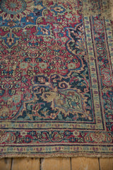 Vintage Meshed rug corner with worn red, blue floral vines and exposed foundation.