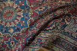 Persian Meshed rug border showing intricate floral vines in dusty red and blue, with visible wear.