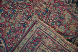 Folded corner of vintage Meshed rug, foundation showing, dusty red, blue palmettes, tattered edge.