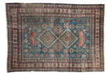 Distressed vintage Caucasian rug with geometric double diamond medallion, dusty blue, red tones.