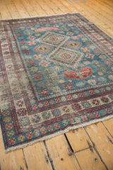 Distressed Caucasian rug corner with worn dusty blue, brick red geometric motifs and short fringe.