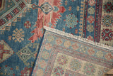Distressed blue and red Caucasian rug pile folded to reveal its detailed woven back and fringe.