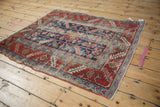 Antique Heriz rug with indigo field, cherry red serrated leaf border, and wear.