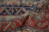 Antique Heriz rug detail: wide red and indigo border, blush floral motifs, visible pile wear.