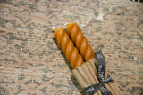 Terra cotta rope beeswax taper candles, partially wrapped, resting on an intricate vintage textile.