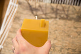 Natural beeswax house candle held in hand, highlighting its warm color and chimney.