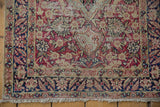 Distressed antique Kerman rug corner, showing worn foundation beneath cochineal red floral vinery.