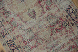 Distressed pile of the antique Kerman runner with cochineal red and navy floral patterns.