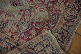 Fringed end of a distressed Kerman runner, revealing worn red and blue floral motifs.