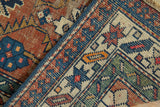 Vintage Caucasian rug showing worn madder red pile, exposed foundation, indigo blue geometric patterns.