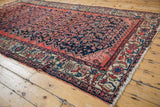 Angled view of a vintage Malayer carpet highlighting its worn texture and detailed floral border.
