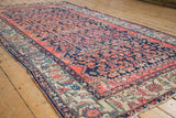 Angled view of a vintage Malayer carpet highlighting its textured Herati motif and worn edges.
