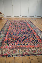 Vintage Persian Malayer carpet seen from an angle, highlighting its tattered sides and low pile.