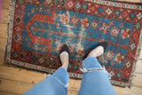Vintage Caucasian rug detail showing indigo blue prayer design, red motifs, and visible wear.