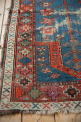 Worn indigo blue pile, geometric red border, and fraying edge of vintage Caucasian rug.