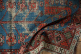 Folded vintage Caucasian rug, showing indigo blue floral motifs and red geometric border with wear.