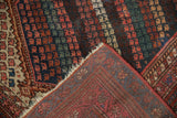 Kurdish rug corner shows ruby red boteh pile, wear exposing knot heads, and woven foundation.