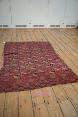 Vintage Turkmen rug corner with geometric gul, pomegranate border, tattered edges, and madder red tones.