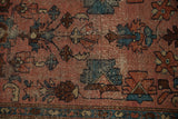 Detail of a vintage Lilihan rug with dusty rose field, blue motifs, and geometric crab border, showing wear.