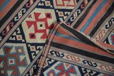 Folded detail of antique Caucasian Kilim: geometric serpent motifs in navy, red, and ivory.