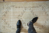 Worn pile and faded pattern of a distressed Oushak rug in cream and coffee brown.