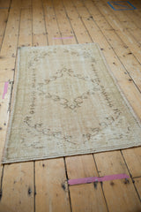 Distressed Oushak rug corner with faded coffee brown patterns and foundation showing.