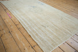 Angled lengthwise view of a distressed Oushak rug highlighting its abrashed beige and ivory texture.