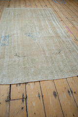 Angled view down the abrashed, sand-colored field of a vintage distressed Oushak rug.