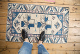 Feet on distressed vintage Oushak rug, with finned geometric patterns in ivory and denim blue.