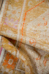 Distressed Oushak rug pile texture showing saffron, tangerine, and violet floral motifs.
