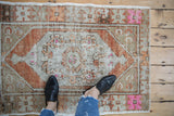 Vintage distressed Oushak rug corner with pale rust and vivid pink geometric motifs.