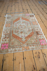 Distressed vintage Oushak rug corner showcasing pale rust geometric spandrel and hot pink floral motifs.