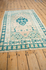 Distressed Oushak rug corner: dusty teal starburst and potted vase borders with fringe.