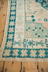 Distressed Oushak rug corner with starburst and rhythmic vase borders in dusty teal and ivory.
