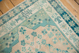 Distressed vintage Oushak rug corner showing starburst and potted vase borders with soft teal floral elements.