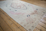 Distressed Oushak carpet section showing abrash, dusty mauve medallion outline, and ivory field.
