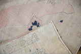 Distressed Oushak texture in dusty pink, folded revealing woven foundation and reverse numbers.