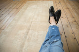 Distressed vintage Oushak runner with faded ivory floral medallions and textured pile wear.