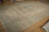Distressed vintage Oushak carpet with faded floral motifs in ivory and seafoam, showing foundation.