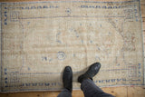 Distressed ivory Oushak rug pile with worn areas and faded blue patterns.