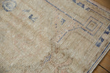 Distressed Oushak rug's worn beige pile, featuring cobalt blue geometric patterns and faded rose.