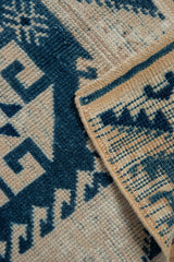 Distressed Oushak rug's folded edge, displaying side cord selvage and geometric navy, beige pattern.