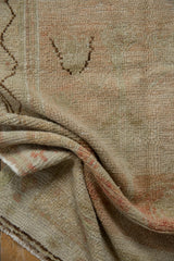 Folded vintage distressed Oushak rug detail, showing soft ivory, blush pile and fringe.