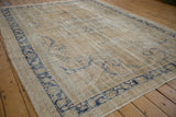 Distressed vintage Oushak carpet showing faded blue scrolling patterns on an abrashed cream field.
