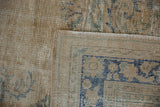 Folded vintage Oushak carpet corner, revealing distressed cream pile, cobalt blue pattern, woven back, and fringe.