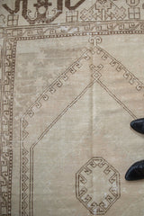 Distressed vintage Oushak rug, geometric brown border, ivory field, and serpent design.