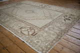Distressed Oushak rug, ivory field with chocolate geometric border and hook-and-latch motifs.