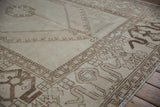 Distressed vintage Oushak carpet showing geometric chocolate border motifs on antique ivory.