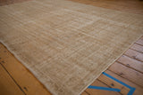 Beige distressed Oushak carpet with aged texture, subtle motif, and diagonal striations.